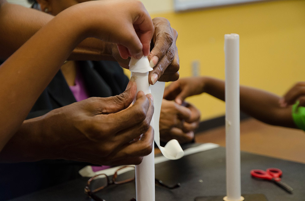 Several hands help build a paper rocket during a Perot Museum Tech Truck stop at the Park and Woods Rec Center in Dallas.