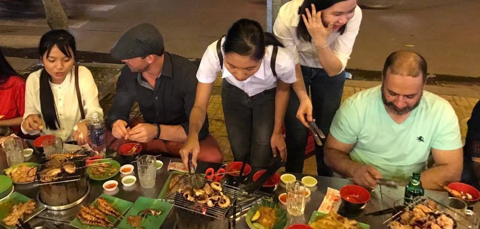 EMBA and GLEMBA students at a street food vendor being shown how to grill their dinner.