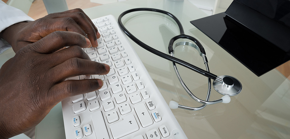 Close-up Of Male Doctor Hands Typing On Computer Keyboard At Desk