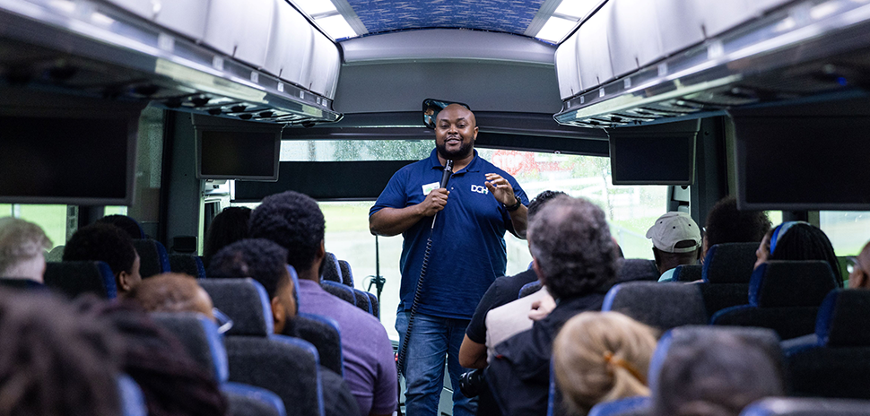 Taken from the back of the bus, shows a developer standing at the front, speaking into a microphone.