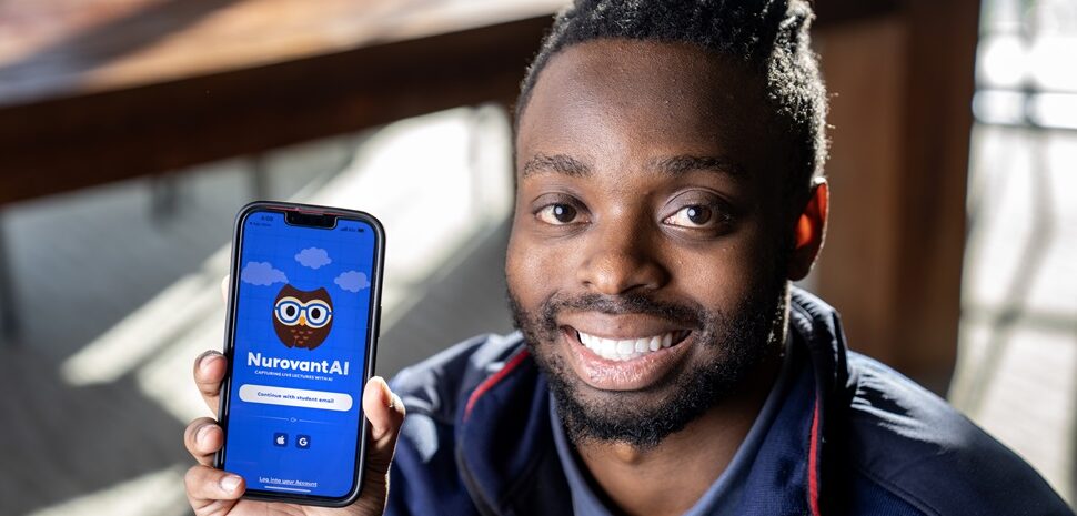 SMU student-entrepreneur Trevor Gicheru, smiling, and posing next to the study app he created.