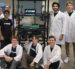John Lauer (left) and members of the Adom Industries team gather around the company’s “workcell”—the core of its cloud-connected electronics prototyping factory. Lauer likens the system to “compute for atoms,” much like a server in a data center enables “compute for bits,” calling it the Amazon Web Services of electronics prototyping. The photo was taken shortly after a major presentation to a leading electronics company, following months of preparation.